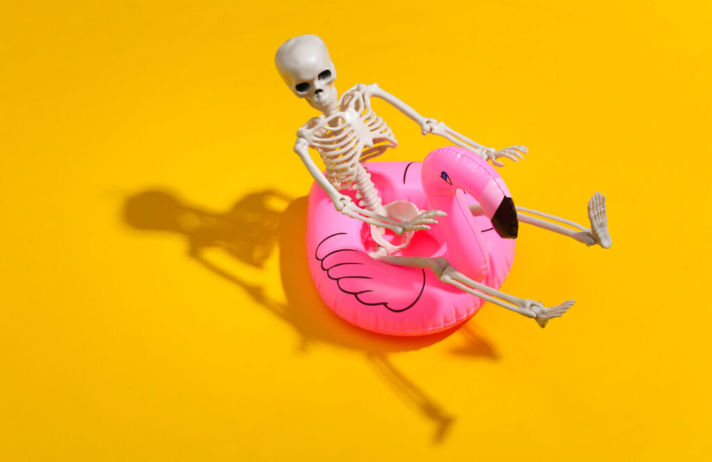 toy skeleton with inflatable flamingo on yellow bright background. halloween theme. beach vacation concept. summer rest.